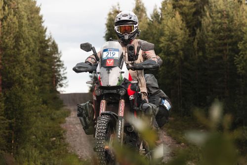 Rider in helmet and gear on a dirt bike, traversing a forest trail.